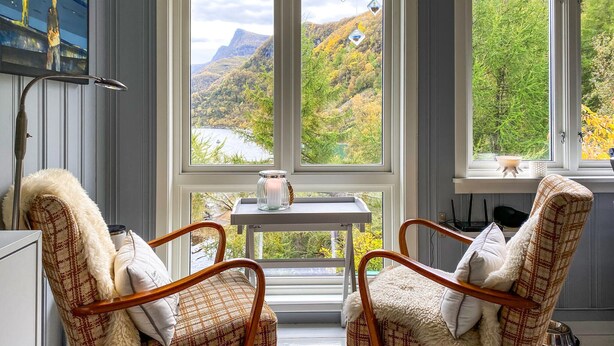 Una habitación acogedora con dos sillones de mimbre, una mesita con una vela y vistas a un paisaje montañoso a través de amplios ventanales.