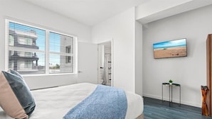 A bedroom with a large bed, a window with blinds, a painting of a beach, and a small table with a plant. - Pool, Terrace & ATM Onsite! Prime Miami Studio nr Beaches (Miami)