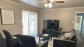 Una sala de estar moderna con un televisor de pantalla plana, dos sofás, una mesa de centro y un ventilador de techo.