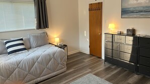 Un dormitorio con cama, lámparas de noche, una puerta de madera, un aparador y un cuadro del océano.