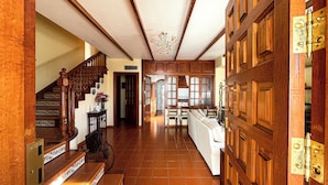 A spacious hallway with a wooden staircase, a kitchen area with a dining set, and a large wooden door. - Villas el Alto (Moya)
