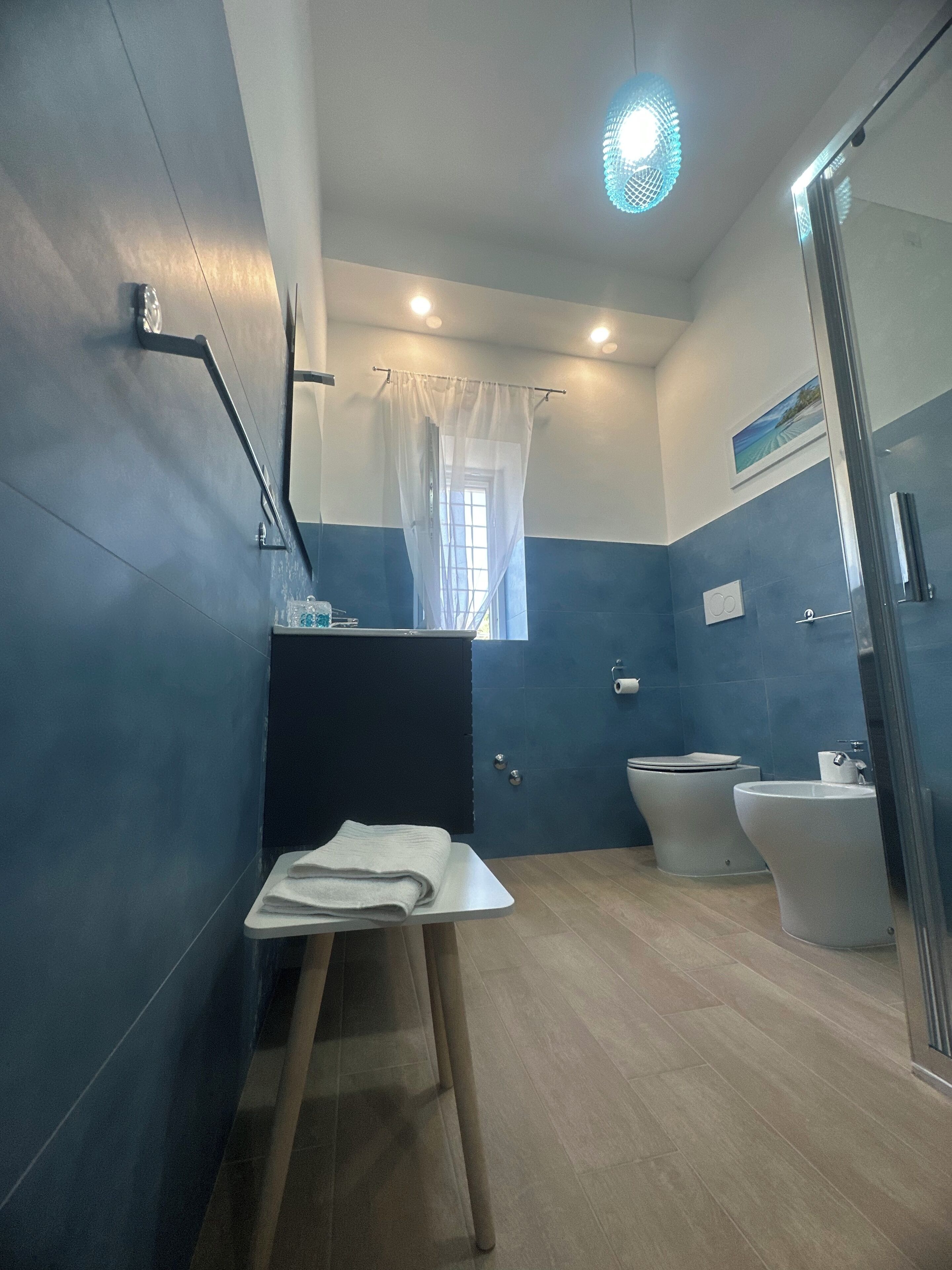 Casa de banho com esquema de cores azul e branco, zona de duche, sanita e lavatório.