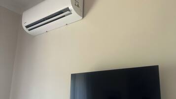 Un equipo de aire acondicionado blanco montado en una pared, con un televisor de pantalla plana debajo.
