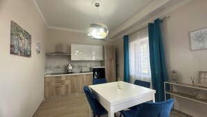 Cocina compacta con armarios blancos, un lavamanos y una estufa. Hay una mesa de comedor con sillas azules y un mantel blanco.