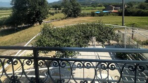 Un balcón con barandillas de hierro forjado que da a un paisaje rural con colinas, árboles y un cielo azul despejado.
