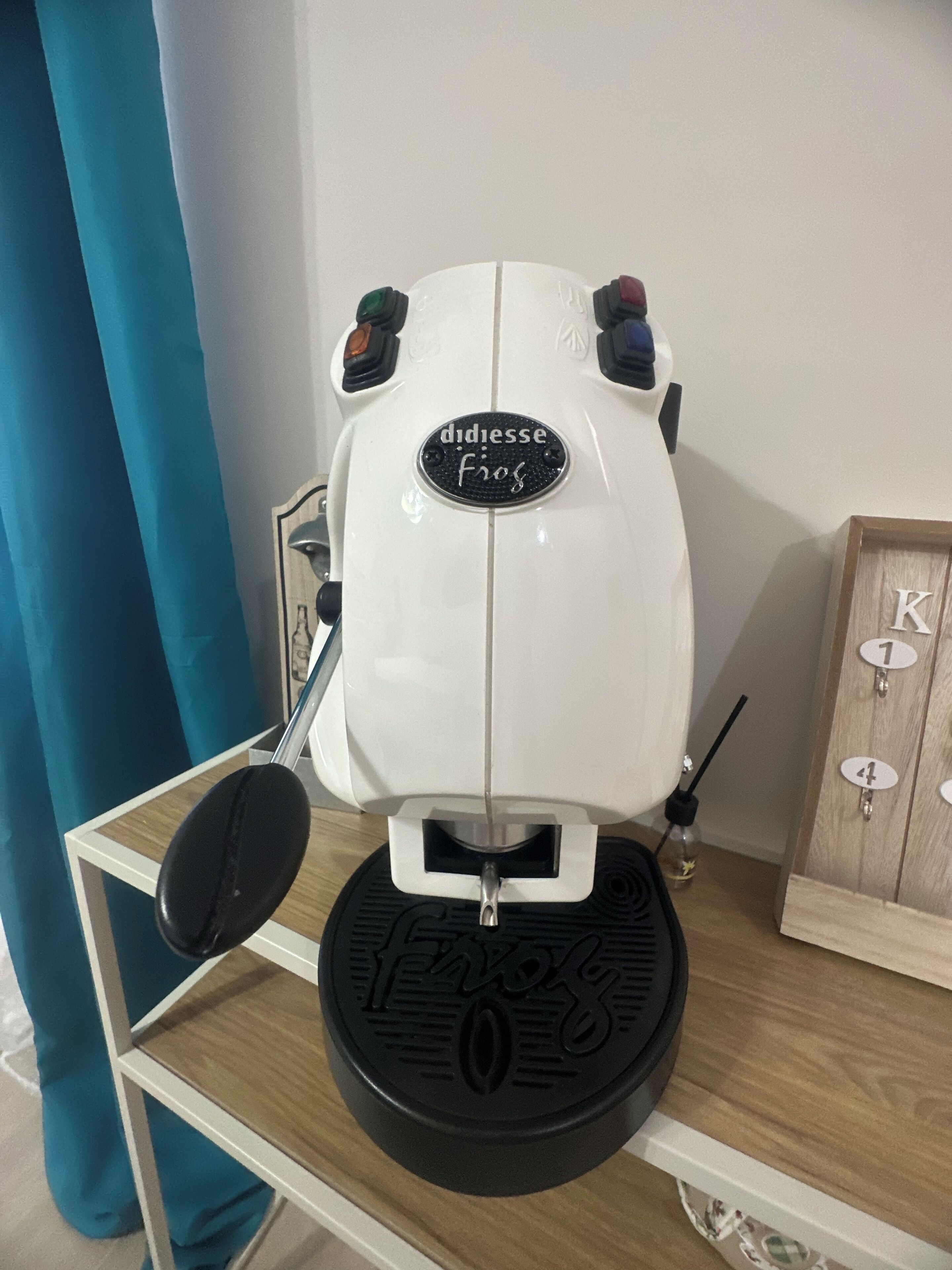 Une trottinette électrique blanche avec une base noire, une plaque signalétique portant l’inscription « didiesse Frogs », et un petit objet noir placé sur le dessus.