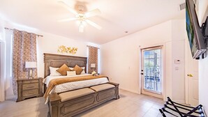 Une chambre dotée d’un grand lit, d’un ventilateur de plafond, d’une table de chevet, d’un téléviseur fixé au mur et d’une porte-fenêtre coulissante donnant sur un balcon.