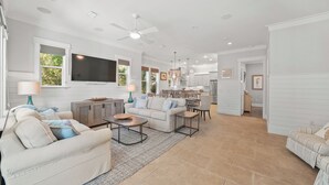 A spacious living room with a large TV, comfortable seating, and a kitchen in the background. - Sandy Bottoms | Inlet Beach Home 5 Minute Walk to Beach & Private Community Pool (Inlet Beach)