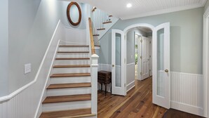 Un escalier avec des marches en bois et des rampes blanches, menant à une pièce dotée d’une porte blanche et d’une petite table en bois.