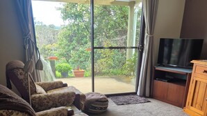 A living room with a sofa, a television, and a sliding glass door leading to a garden. -  Nannup Riverview Cottage, fully Self Contained Holiday Let (Nannup)