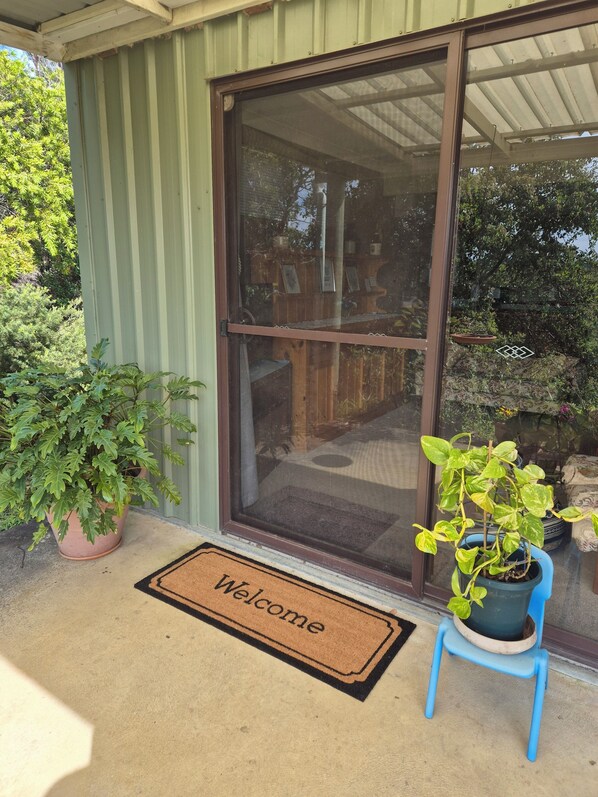 A house entrance with a sliding glass door, a welcome mat, and potted plants on the porch.