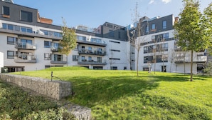A modern apartment complex with multiple balconies, a grassy courtyard, and a stone retaining wall. - Royal Wilanów Chic Studio (Warszawa)