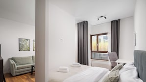 A modern hotel room with a bed, a sofa, a window with curtains, and a view of greenery outside. - Royal Wilanów Chic Studio (Warszawa)