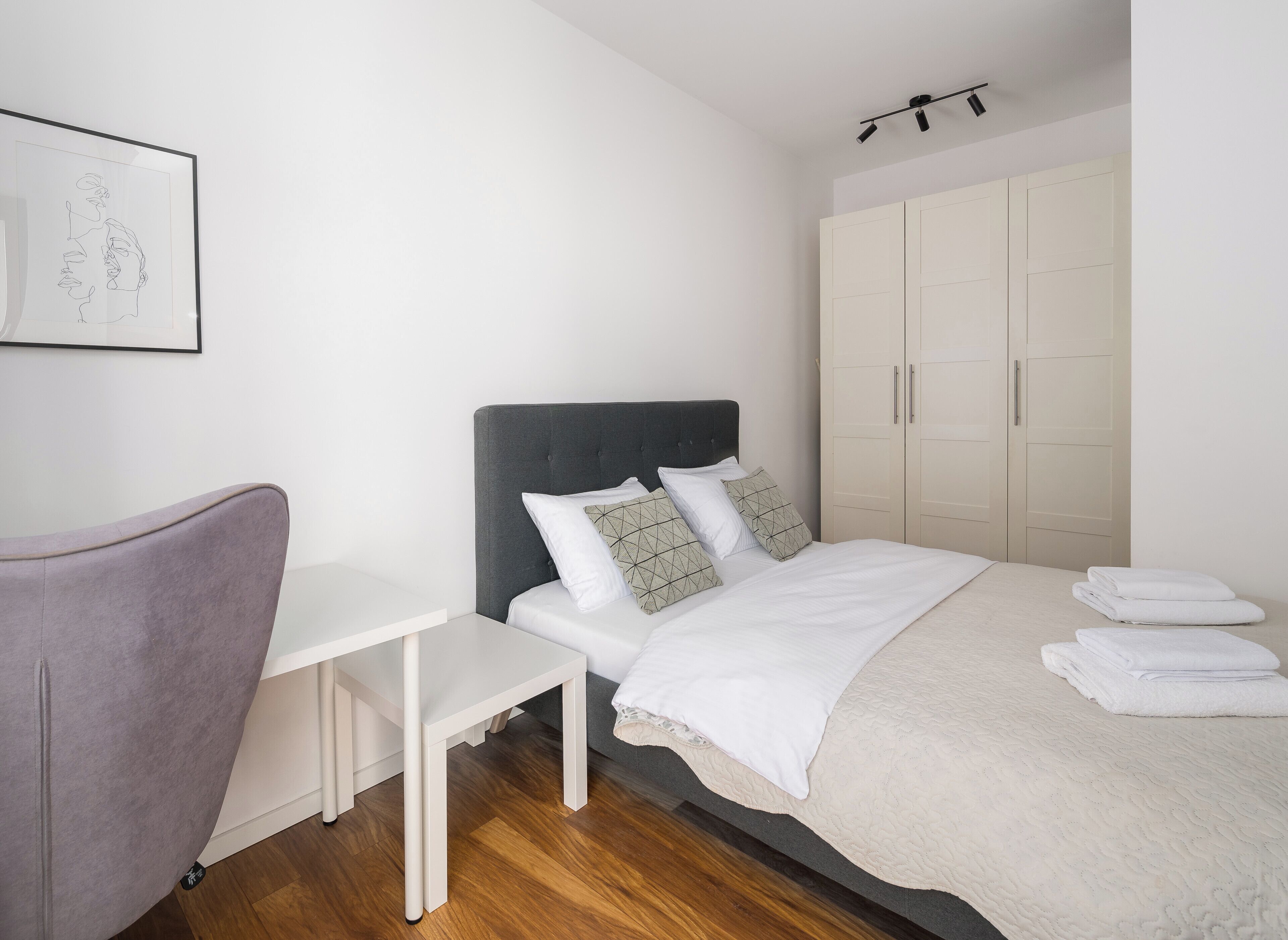 Un dormitorio ordenado con cama, mesita de noche, silla y armario.