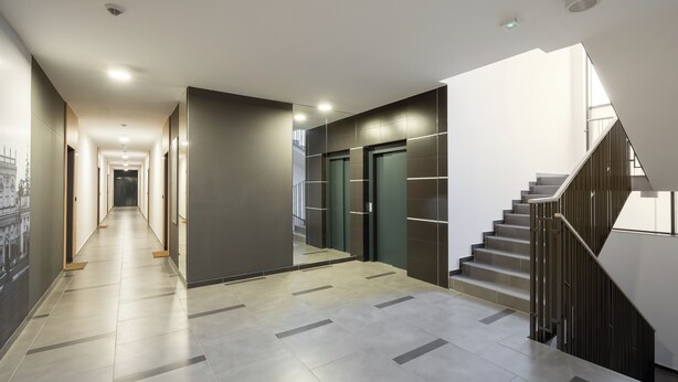 A modern hotel hallway with a staircase, a long corridor with doors, and a tiled floor. - Royal Wilanów Chic Studio (Warszawa)