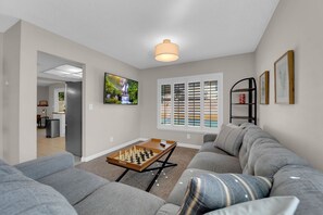 A living room with a sofa, a coffee table, a TV, and a window with blinds.