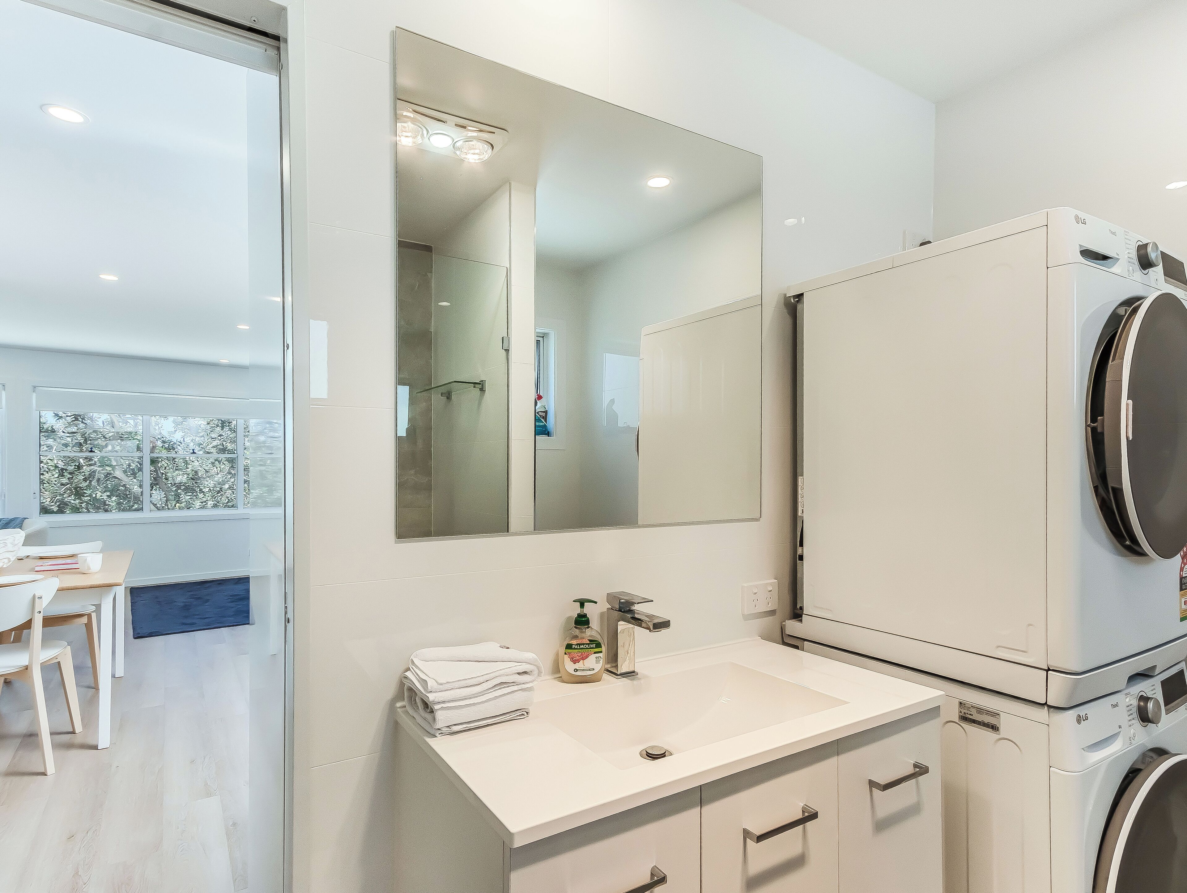 A modern bathroom with a large mirror, a sink, and a washing machine.