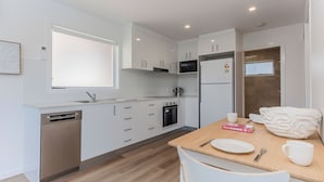 Una cocina moderna con armarios blancos, lavavajillas de acero inoxidable, horno empotrado y refrigerador.