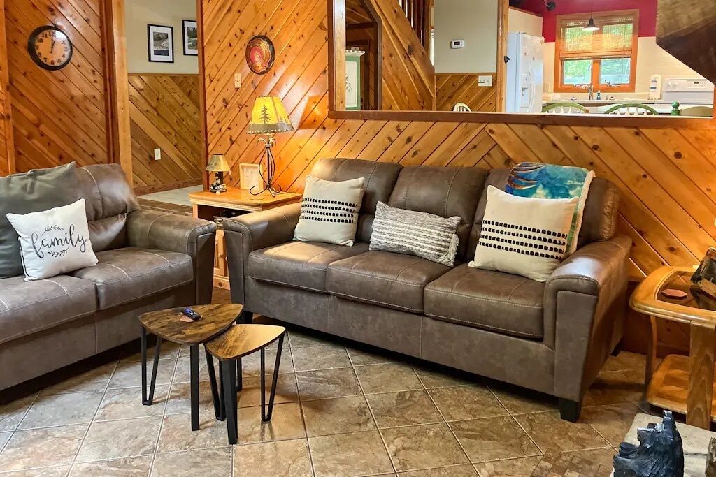 Un salón acogedor con un sofá de cuero marrón, dos sillones a juego, una mesita de centro de madera y una lámpara en una mesita auxiliar.