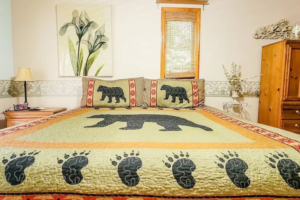 Une chambre à coucher avec un grand lit, une table de chevet, une lampe, une fenêtre et un meuble décoratif.