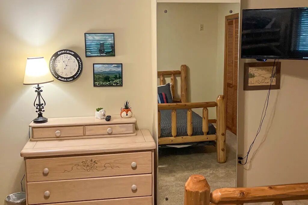 Une pièce comprenant une commode en bois, une horloge murale, des tableaux encadrés, un téléviseur et une chaise en bois.