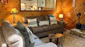 Un accogliente soggiorno con un divano in pelle marrone, un divano più piccolo e un tavolino da caffè. Sopra il divano c'è uno specchio, una lampada a sinistra e un cartello appeso al muro con la scritta CABIN.