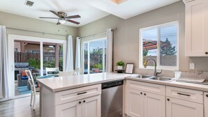 A modern kitchen with white cabinets, a dishwasher, and a large window with an umbrella. - Serenity Villa Hermosa, Jacuzzi, Arcade & Fun Games, Backyard, Outdoor Furniture (Moreno Valley)