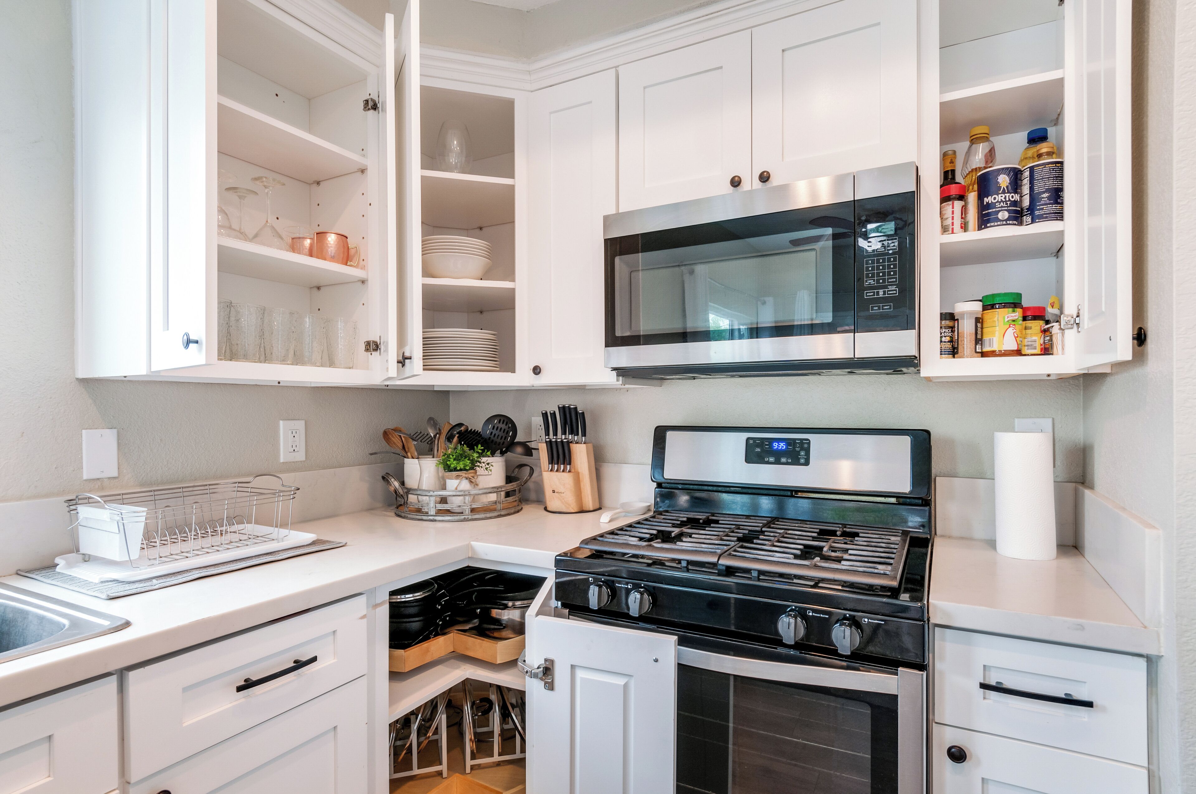 A kitchen with white cabinets, a stainless steel stove, a microwave, and various kitchen utensils.