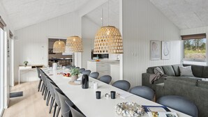 A spacious kitchen with a long dining table, modern pendant lights, and a view of the outdoors.