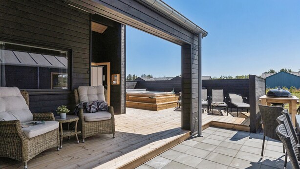 A covered outdoor seating area with wicker furniture and a hot tub.