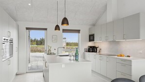 A modern kitchen with white cabinetry, a large island, and a view of a natural landscape through the windows.