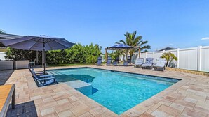 Ein rechteckiger Pool mit Fliesenränder, umgeben von Liegestühlen und Sonnenschirmen.