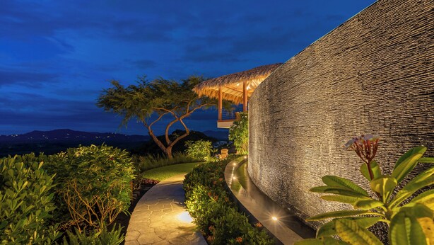 A pathway leading to a building with a textured wall and a thatched-roof structure. - Stunning Brand New Villa with Ocean & Mountain Views, Just a Minute's Drive to Tamarindo Beach (Tamarindo)