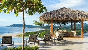 A beachside lounge with a thatched roof, outdoor seating, and a view of the ocean and hills. - Stunning Brand New Villa with Ocean & Mountain Views, Just a Minute's Drive to Tamarindo Beach (Tamarindo)
