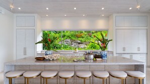 Uma cozinha moderna com uma ilha grande, banquetas e vista para um jardim exuberante.