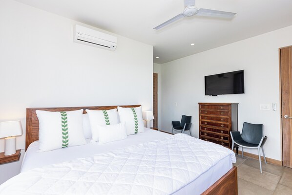 Habitación de hotel con cama, televisor montado en la pared, cómoda y una silla.