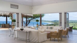 Ampla sala de estar com uma grande janela com vista para o mar e colinas.