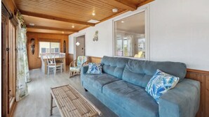 A cozy living room with a blue sofa, a wooden bench, and a dining area with a table and chairs. - Tiki Tides OBX 4-Bedroom Beach Box in Kill Devil Hills, Steps from the Beach! (Kill Devil Hills)