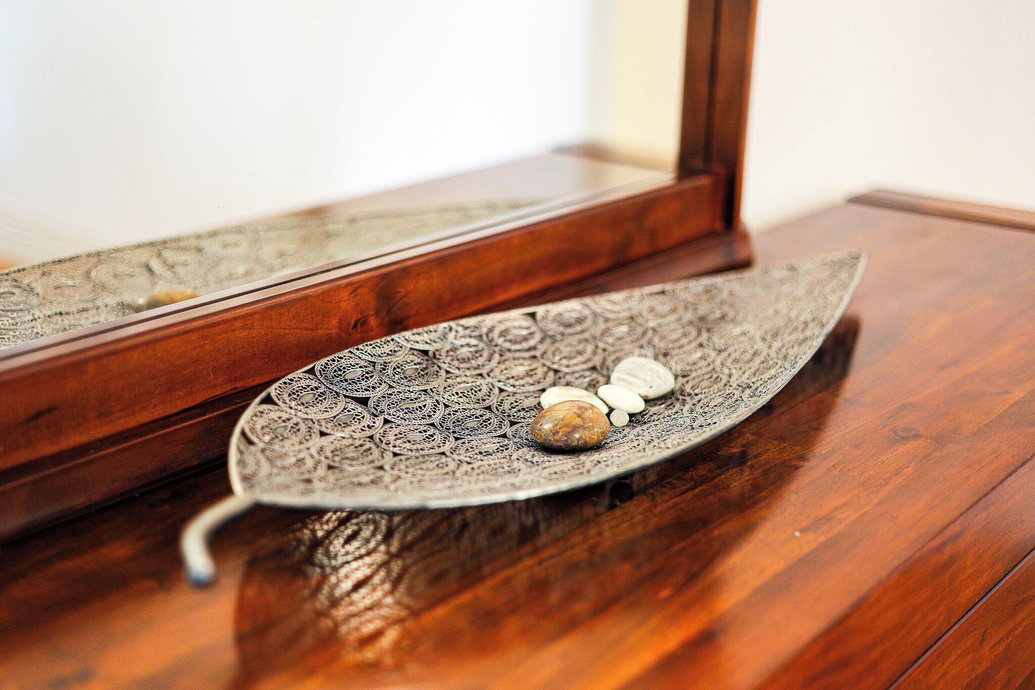 A wooden table with a decorative metal tray featuring intricate patterns and a few stones.