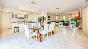 A spacious kitchen with white cabinets, a central island, and a dining area with a glass table and white chairs. - StayAU Expansive 7BR Villa Warrandyte (Warrandyte)