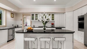 A modern kitchen with white cabinets, a black countertop, and a central island with bar stools. - StayAU Expansive 7BR Villa Warrandyte (Warrandyte)