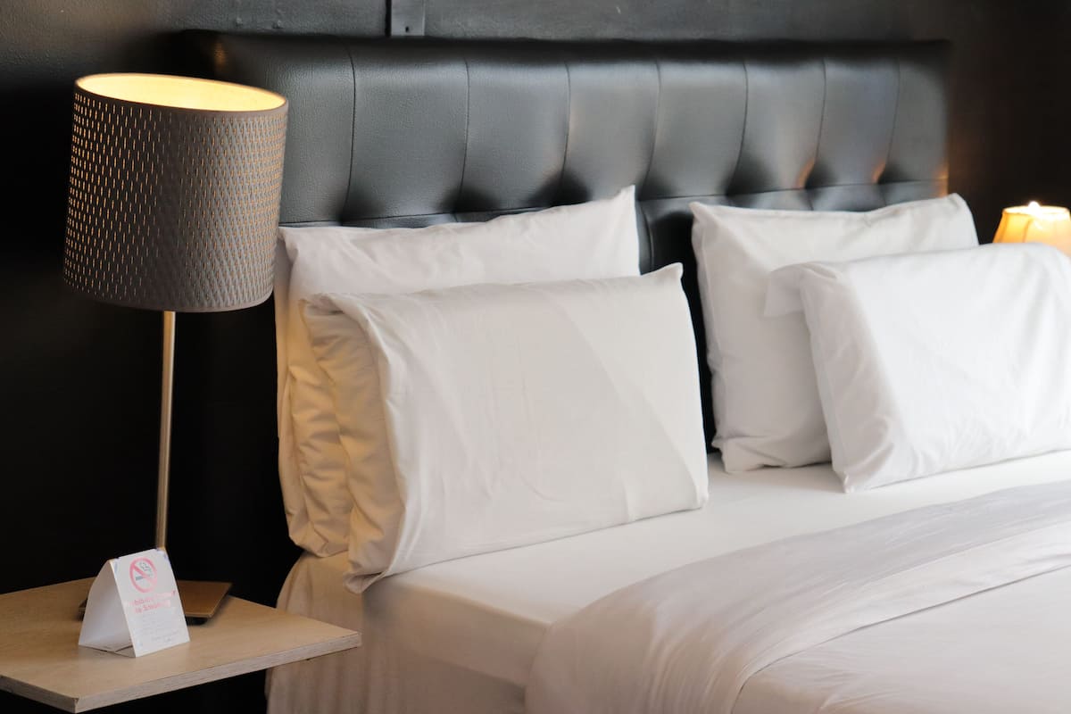 Un lit bien fait, avec du linge de lit blanc, une tête de lit noire en tissu et une lampe sur une table de chevet.