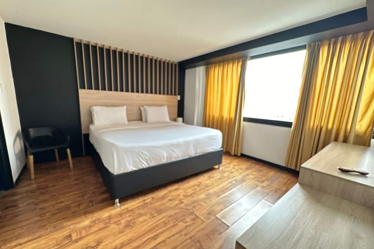 Une chambre d’hôtel moderne, dotée d’un grand lit, d’un petit bureau et offrant une vue sur l’extérieur grâce à une fenêtre avec des rideaux.