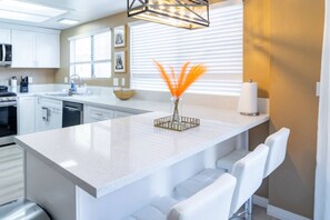A modern kitchen with white cabinetry, a central island with bar stools, and a decorative vase with orange feathers.