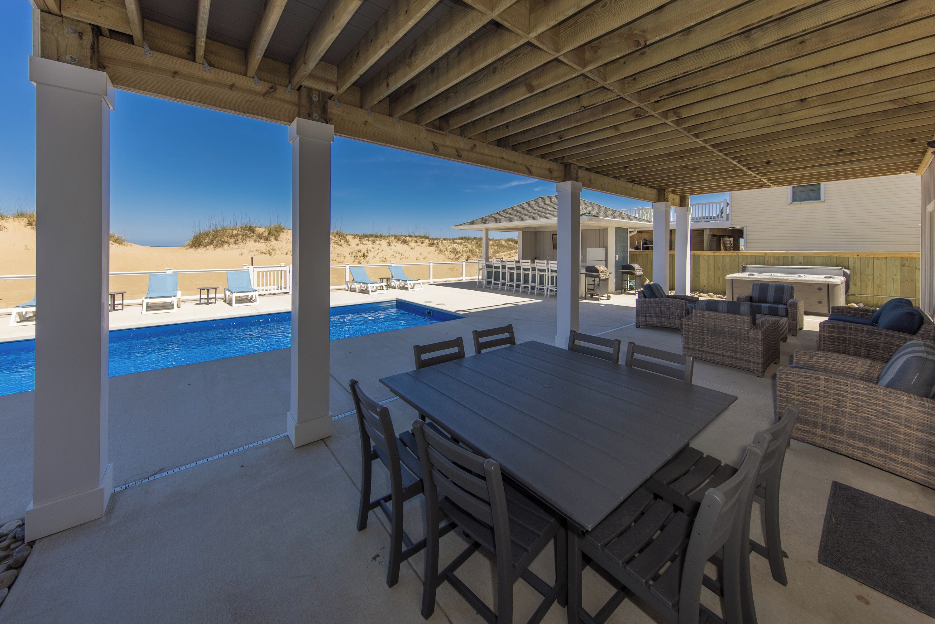 A covered outdoor area with a pool, dining table, and lounge chairs.