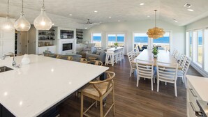 Une cuisine spacieuse avec un grand îlot central, des chaises en bois et une vue sur l’océan.