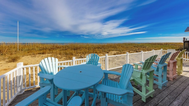 Eine Terrasse mit Tisch und Stühlen mit Blick auf einen Strand.