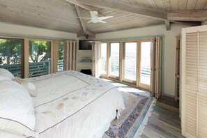 Un dormitorio con una cama grande, ventilador de techo, televisor y vistas al exterior.