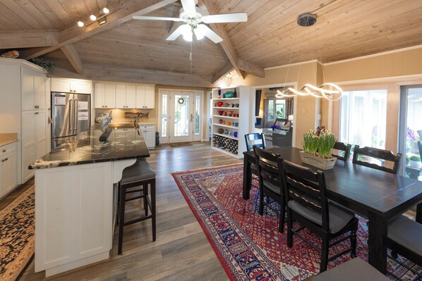 A spacious kitchen with a large island, wooden ceiling, and a dining area with a red patterned rug. - OCEANFRONT - Great views, Hot Tub, Sleeps 9 (Virginia Beach)