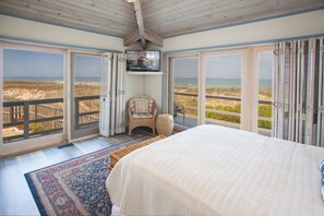 A bedroom with a large bed, a television, and a view of the beach through open sliding doors. - OCEANFRONT - Great views, Hot Tub, Sleeps 9 (Virginia Beach)